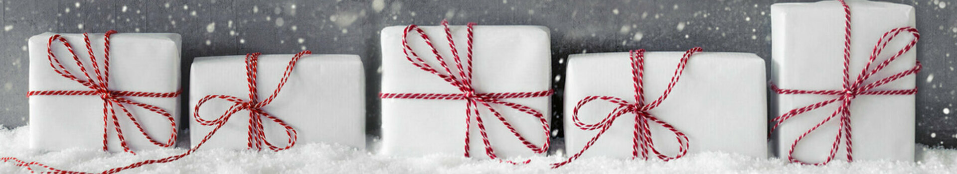 ATLANTIC Hotels Gutschein-Shop Weiße Geschenke mit roten Schleifen im Schnee vor grauem Hintergrund mit fallenden Schneeflocken.