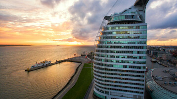 ATLANTIC Hotel Sail City – Außenansicht ATLANTIC Hotel Sail City in Bremerhaven, bei Sonnenuntergang am Wasser, mit modernem, gebogenem Glasdesign.