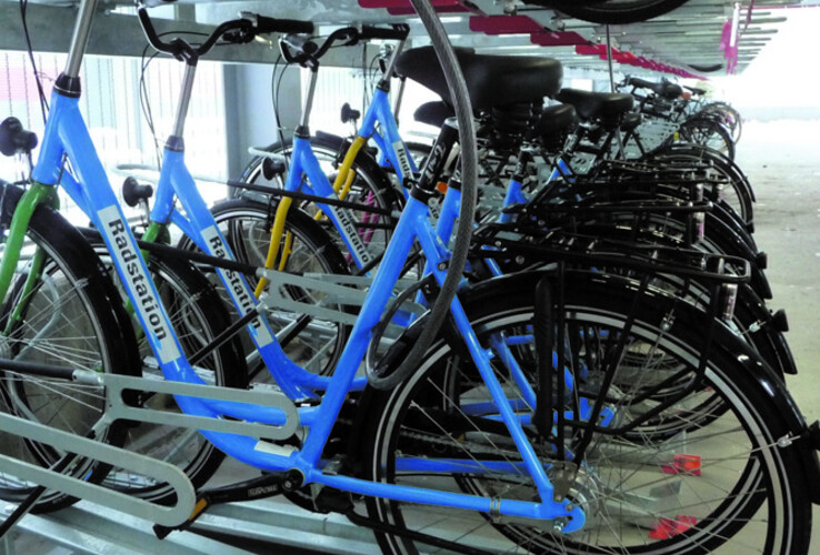 Bicycles in blue frames stand neatly in a two-story bike rack in an interior room.