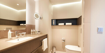 Modernes Hotelbad mit großem Spiegel, Waschtisch, Handtüchern und WC in warmen Tönen, stilvoll und gut beleuchtet.