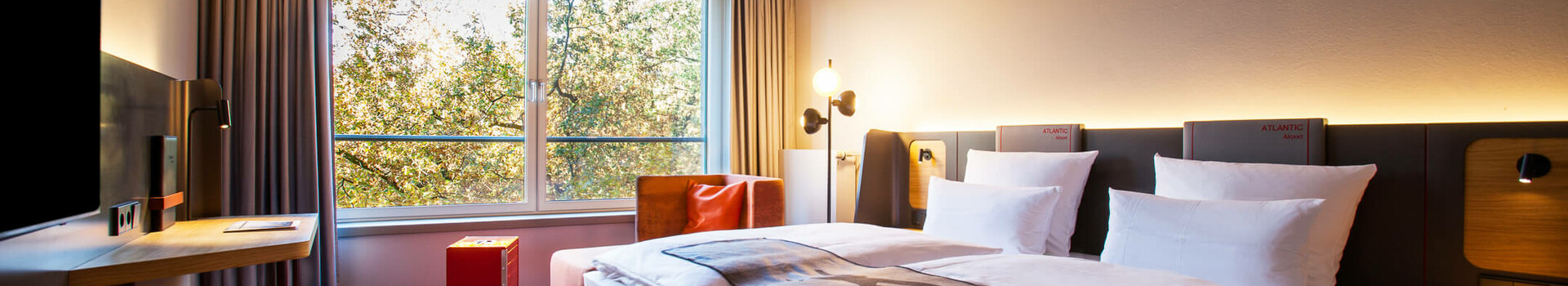 Business Zimmer im ATLANTIC Hotel Airport Modernes Hotelzimmer mit Doppelbett, Schreibtisch, großem Fenster und Decke mit Wolkenmotiv im ATLANTIC Hotel Airport Bremen.