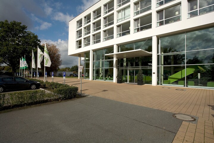 Parking in front of the ATLANTIC Hotel Galopprennbahn in Bremen Modern hotel entrance with glass façade, several flags and parking lot at the ATLANTIC Hotel Galopprennbahn in Bremen.