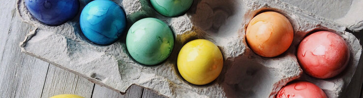 Bunte, gefärbte Ostereier in einer Eierkartonverpackung auf Holzoberfläche.