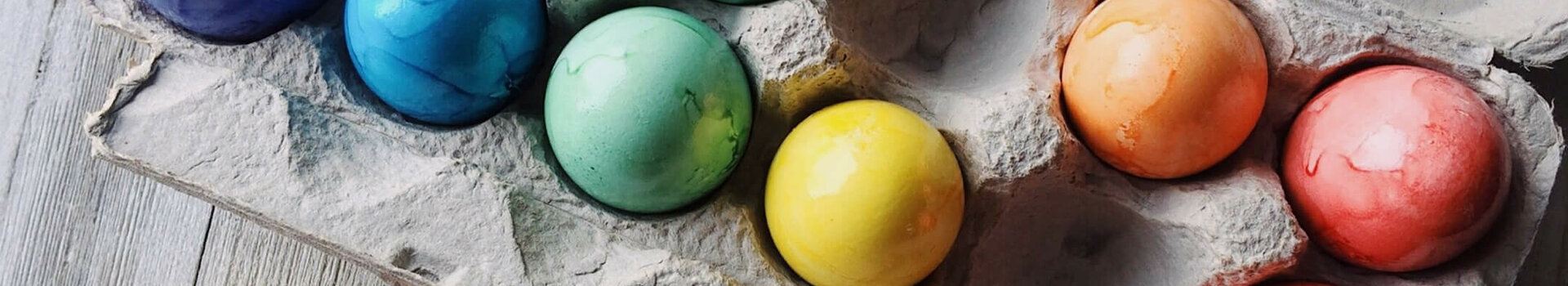 Colorful, dyed Easter eggs in an egg carton packaging on a wooden surface.