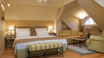 ATLANTIC Grand Hotel Travemünde double room Cozy hotel room with double bed, striped sofa, armchair, table with fruit and elegant lighting.