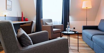 Gemütliche Sitzecke im ATLANTIC Hotel Landgut Horn mit Sofa, Sesseln, Tisch mit Wasserflasche und Stehlampe.