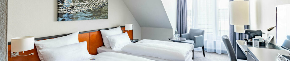 ATLANTIC Hotel Vegesack Comfort Doppelzimmer Helles Hotelzimmer mit zwei Einzelbetten, modernem Dekor und großem Fenster im ATLANTIC Hotel Vegesack, Bremen.