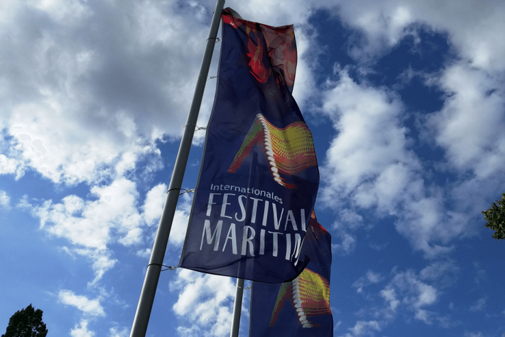Flagge des Internationalen Festival Maritim vor blauem Himmel mit Wolken.