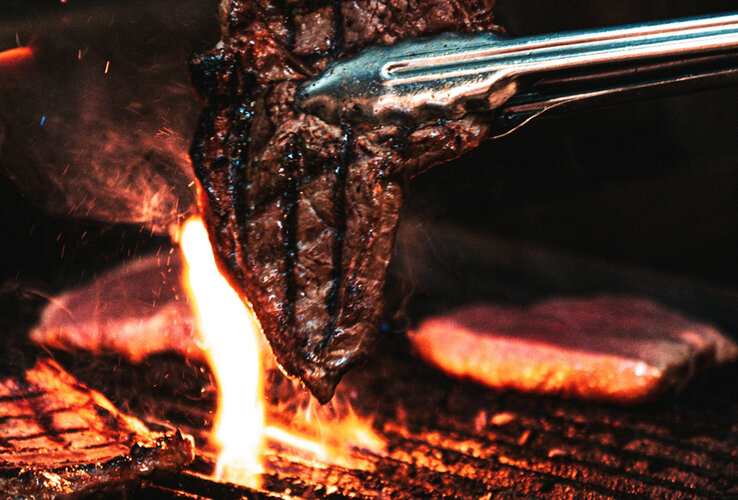 Steak wird auf einem Grill gewendet.