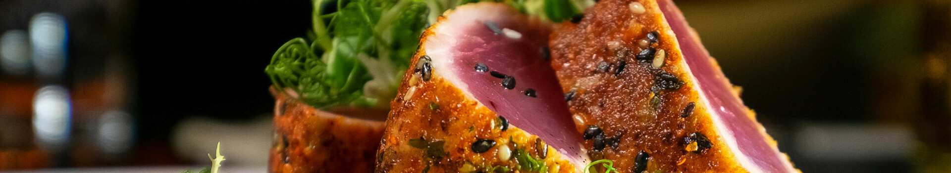Header Meal ATLANTIC Grand Hotel Bremen Close-up of juicy tuna in a crispy sesame crust, decorated with fresh herbs.