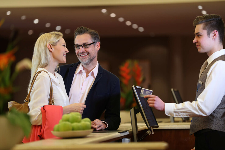 Paar checkt an der Rezeption des ATLANTIC Grand Hotel Travemünde ein, freundlicher Empfang durch Hotelmitarbeiter.